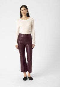 Tricou cu mânecă lungă, de culoare bej deschis, asortat cu pantaloni strâmți din piele ecologică burgundă. Pantalonii au o tăietură evazată la tiv. Pantofi negri slip-on finalizează ținuta.