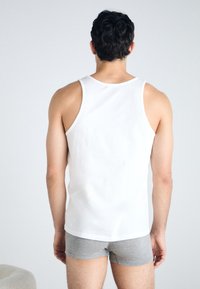 Weißes Baumwoll-Top mit breiten Trägern, kombiniert mit grauen Shorts. Einfaches Design mit glatter Textur und ohne sichtbare Muster oder Logos.