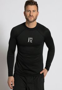 Schwarzes langärmeliges Performance-Shirt mit taillierter Passform, aus dehnbarem Material, mit einem weißen Grafikdruck auf der Vorderseite.