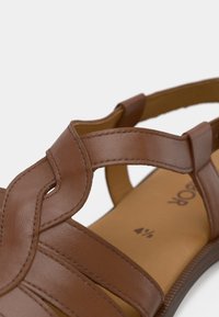 Καφέ δερμάτινο σανδάλι με διασταυρούμενους ιμάντες, ανοιχτό σχέδιο και υφή φινιρίσματος. Ανοιχτό καφέ εσωτερική σόλα με ενδείξεις μεγέθους.