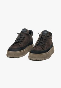 Hnědé semišové boty s černými akcenty, kulatou špičkou, silnou texturovanou podešví a černými tkaničkami. Na jazyku se nachází logo 'estro'.