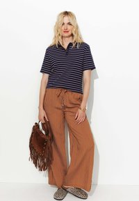 Polo shirt rayé marine, pantalon large rayé marron léger, sac à main à franges marron et slippers à imprimé léopard. Détails de tenue décontractée.