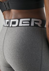 Pantaloni sportivi grigi in tessuto testurizzato, con vita nera caratterizzata da lettere bianche. Il design include cuciture piatte per il massimo comfort.