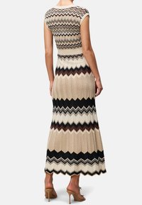 Długa sukienka maxi z dopasowanym gorsetem, krótkimi rękawami i zygzakowatym wzorem w kolorach beżowym, brązowym i czarnym. Prążkowana faktura, rozkloszowany dół.