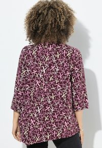 Túnica color marrón con mangas tres cuartos, que presenta un patrón repetido de lazos en rosa, blanco y beige; fabricada con un tejido suave y ligero.