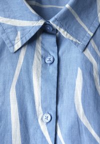 Camicia blu a fantasia con colletto, caratterizzata da strisce astratte bianche e bottoni azzurri chiari. Il tessuto sembra morbido con una superficie liscia.