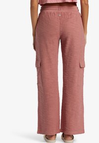 Spodnie o szerokich nogawkach wykonane z teksturowanej, różowej tkaniny. Posiadają elastyczny pas w talii oraz dwie boczne kieszenie typu cargo. Długość sięga prawie do kostek.