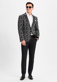 Schwarz-weißes Leopardenmuster-Blazer mit Satinrevers, kombiniert mit schwarzen Hosen und polierten Schuhen. Die Accessoires umfassen runde Sonnenbrillen.