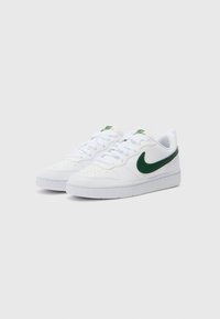 Baskets blanches avec un swoosh Nike vert, présentant une boîte à orteils perforée, des lacets plats et une semelle en caoutchouc blanc. Matériaux en cuir lisse et en textile.