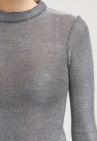 Maglione grigio lavorato a maglia con colletto alto e maniche lunghe, caratterizzato da un motivo testurizzato e un finish semi-trasparente, che mette in risalto il suo materiale leggero.