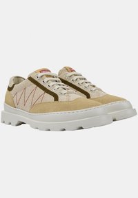 Beige canvas sneakers with a light brown suede accent, featuring a rubber sole, raised white platform, and red logo detailing.