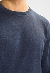 Námořnický modrý sweatshirt s kulatým výstřihem vyrobený z měkkého materiálu, s malým logem v červené, b�ílé a modré barvě na hrudi.
