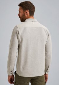 Lichtgrijze shirt met wafelstructuur en lange mouwen, een button-down kraag en contrasterende beige schouderpanels. Voorzien van knoopmanchetten.