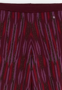 Leggings texturizados con una base en color marrón burdeos y patrones en zigzag en rojo, púrpura y destellos dorados. Presenta una cintura acanalada en la parte superior.