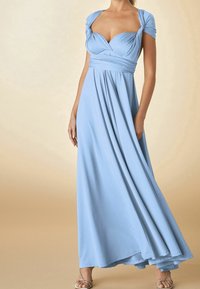 Robe longue bleu clair en tissu doux et froncé, manches courtes, corsage drapé et jupe fluide. Portée avec des sandales argentées à fines lanières.