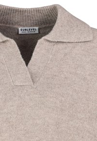 Beige gebreide pullover met een geribde kraag en sluiting. Heeft een textuurstof en een label voor een medium pasvorm. Zachte, casual uitstraling.