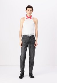 Canottiera bianca a costine, jeans neri con una vita a fantasia e stivaletti neri. Bandana rossa legata attorno al collo come dettaglio decorativo.