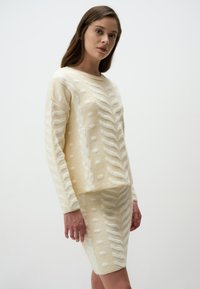 Completo in maglia beige composto da sweater e gonna con texture a rilievo, caratterizzato da un motivo a zigzag e pois. Maniche lunghe e scollatura rotonda.