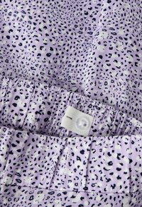 Tissu lilas avec de petites taches léopard noires et blanches, doté d'une ceinture élastique ajustable avec un bouton transparent.