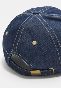 Jeans baseballkeps i mörkblått med kontrasterande beige sömmar. Har en böjd skärm och justerbart band med en metallspänne.
