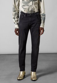 Vaqueros oscuros de mezclilla con un corte ajustado, diseño de cinco bolsillos y una textura ligeramente desgastada, combinados con botas de tobillo metálicas doradas.