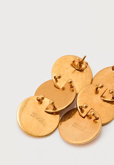 Σετ από χρυσούς κυκλικούς κρίκους stud της Versace με πίσω κλείσιμο push-back, σφραγισμένοι με την ένδειξη "VERSACE MADE IN ITALY", τοποθετημένοι σε λευκό φόντο.