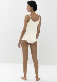 Top in crema con spalline sottili, design aderente e texture morbida, abbinato a slip coordinati, mostrato su un modello visto da dietro.