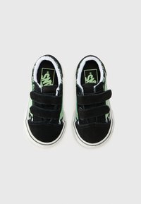 Svarta mockasneakers med gröna detaljer, kardborreband och ett mönstrat innerfoder; rund tå och vit gummisula.