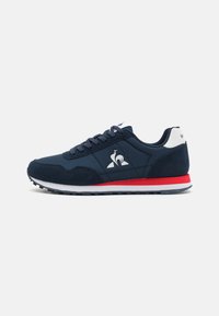 Scarpa da ginnastica navy con un mix di superfici lisce e testurizzate, logo bianco, dettagli rossi sulla soletta intermedia e suola in gomma nera.