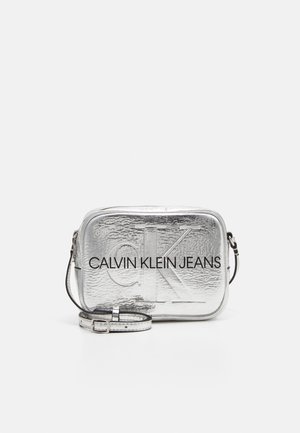 Borsa a tracolla rettangolare argentata con superficie testurizzata. Presenta il logo "CALVIN KLEIN JEANS" in rilievo e una tracolla regolabile.