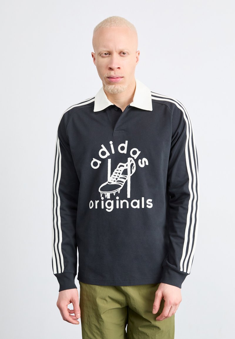 Polo cu mânecă lungă negru cu guler alb și trei dungi albe pe mâneci, având un print grafic cu o încălțăminte și textul "adidas originals."