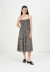 Rochie de vară cu model în nuanțe de negru și bej, cu un corset ajustat, detalii pliate și fustă evazată; asociată cu sandale cu toc bloc negre.