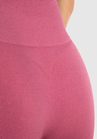 Růžové bezešvé legíny s vysokým pasem, s texturovaným, žebrovaným pasem a hladkým materiálem. Na zadní straně mají jemný trojúhelníkový vzor.