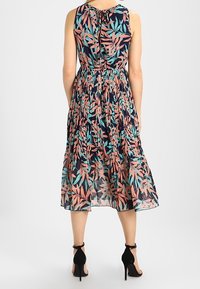 Abito midi floreale con sfondo navy, caratterizzato da motivi di foglie rosa e teal, senza maniche e con dettagli di vita arricciati. Tacchi neri in vista.