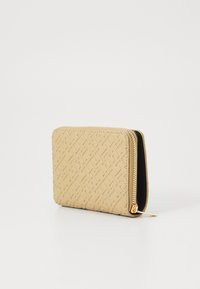 Portefeuille beige texturé avec un motif géométrique, fermeture éclair et quincaillerie dorée. Intérieur noir. Taille compacte et forme rectangulaire.