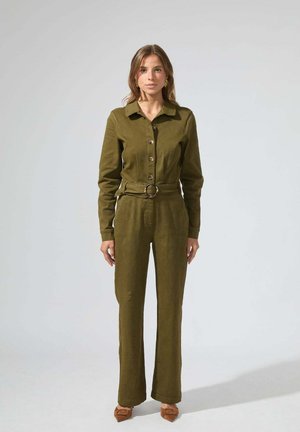 Combinaison vert olive avec un devant à boutons, des manches longues et une ceinture en tissu avec une boucle ronde. Texture lisse, pantalons à jambes larges.