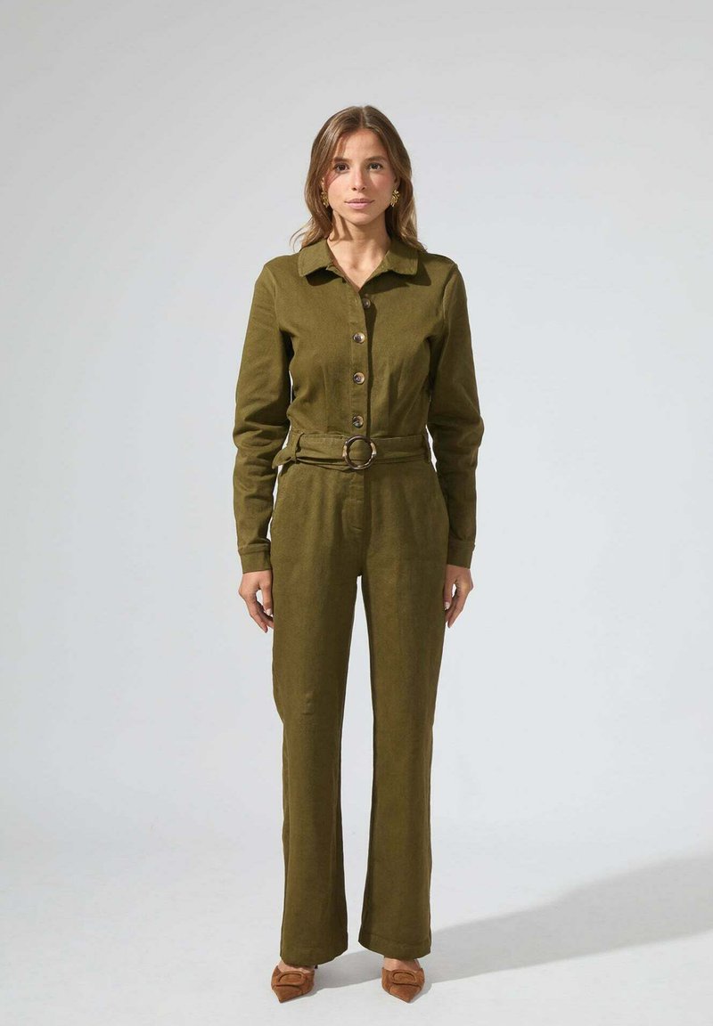 Combinaison vert olive avec un devant à boutons, des manches longues et une ceinture en tissu avec une boucle ronde. Texture lisse, pantalons à jambes larges.