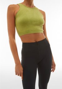 Crop top verde a costine con scollo rotondo, caratterizzato da un design aderente e cuciture a contrasto, abbinato a leggings neri a vita alta con zip.
