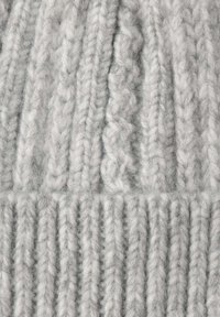 Gorro gris de punto hecho de hilo grueso con una textura acanalada, que presenta patrones alternos de trenzado y rectos para un detalle adicional.