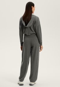 Grå, avslappnad sweatshirt med huva, som sätts ihop med vida byxor. Mjuk textur, ribbade manschetter och en sömlös design. Idealisk för komfort.