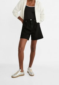 Shorts de mezclilla negra con cintura alta, con bolsillos frontales y cierre de botón. Combinados con una sudadera con cremallera gris y zapatillas plateadas.