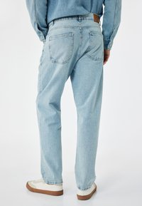 Ljust blå denimjeans med avslappnad passform, med två bakfickor och detaljer i brunt läder på midjebandet. Stylar med vita och bruna sneakers.