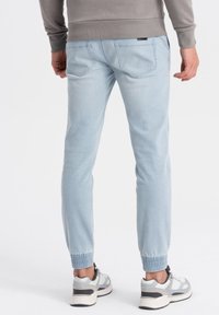 Jasnoniebieskie spodnie dresowe z elastycznym paskiem i mankietami, z przeszytymi tylnymi kieszeniami i miękką teksturą dżinsu. Zestawione z szaro-białymi sneakersami.