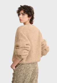 Maglione beige oversize con texture a coste e spalle basse, abbinato a pantaloni crema con stampa a stampa leopardata nera.