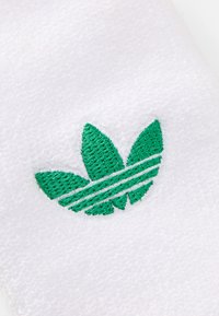 Tecido branco com uma superfície texturizada, apresentando um design de logótipo bordado em verde com três formas semelhantes a folhas e três riscas horizontais.