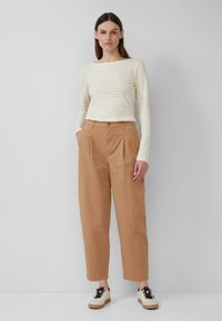 Maglietta a maniche lunghe a righe in crema e giallo pallido, abbinata a pantaloni beige a vita alta con pieghe e scarpe stringate bicolore nere e beige.