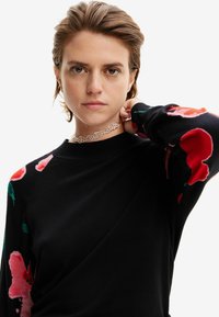 Maglione nero con motivi floreali in rosa e rosso sulle maniche, con scollatura tonda e una texture liscia. Accessorio choker in argento.
