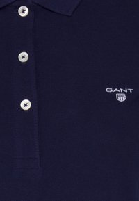 Mörkblå polo skjorta i texturerat tyg. Har en klassisk krage, två framknappar och en liten vit GANT-logotyp på bröstet.