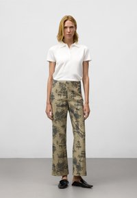 Witte polo met korte mouwen en kraag, gecombineerd met brede beige broeken met een blauw stippenpatroon, afgewerkt met zwarte instappers.