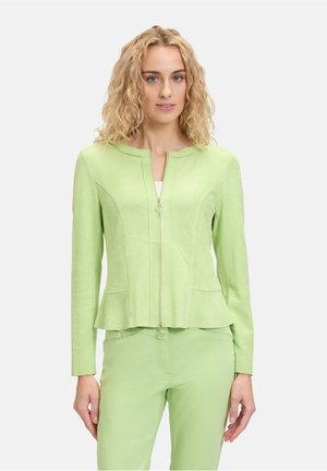 Light green zip-up jacket with a peplum design, smooth texture, and two front pockets. Styled with matching green trousers.